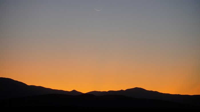 Crescent moon over silhouetted mountains at sunset