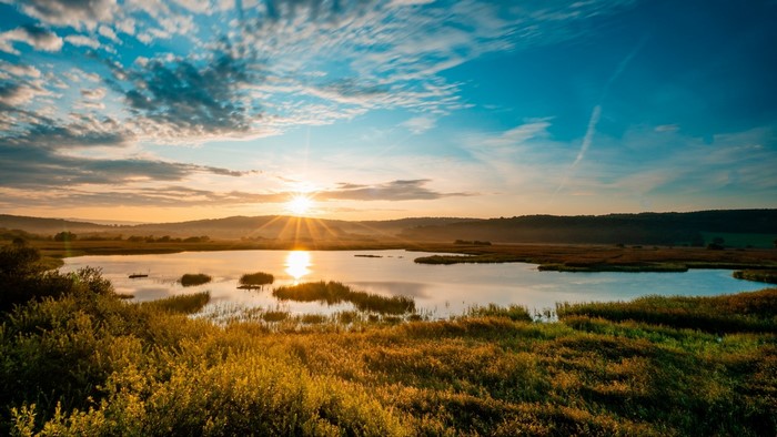Sunrise over a lake with reeds and hills