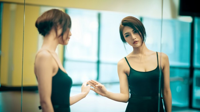 Asian model in black dress looking in mirror
