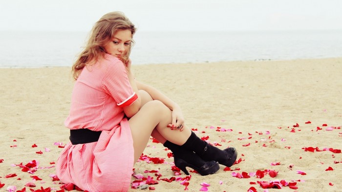 Woman in pink dress sitting on beach with rose petals