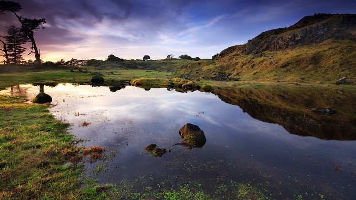 Pond reflecting hills and trees at sunset