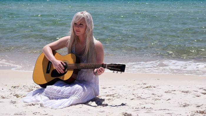 Blonde girl playing guitar on a beach