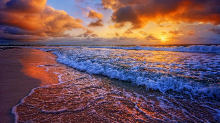 Sunset over ocean waves on a sandy beach