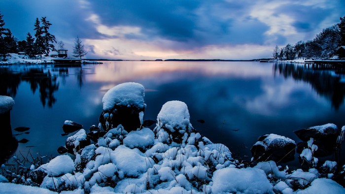 Snowy lake with trees and a dock at dusk