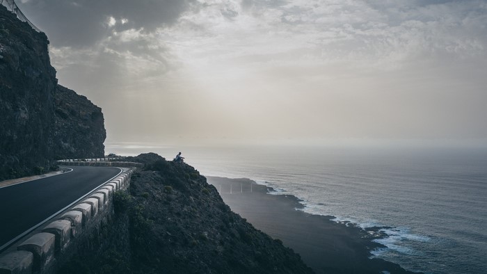 Person sitting on a cliff overlooking the ocean