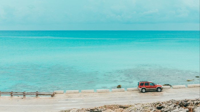Red SUV parked by turquoise ocean on a sunny day