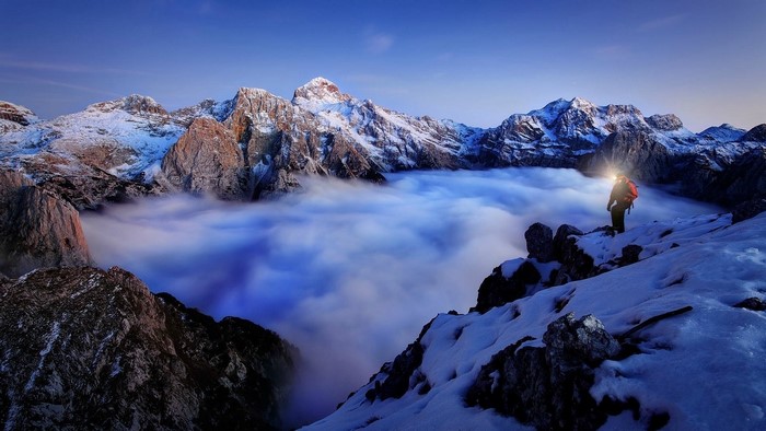 Climber with headlamp in snowy mountains above clouds