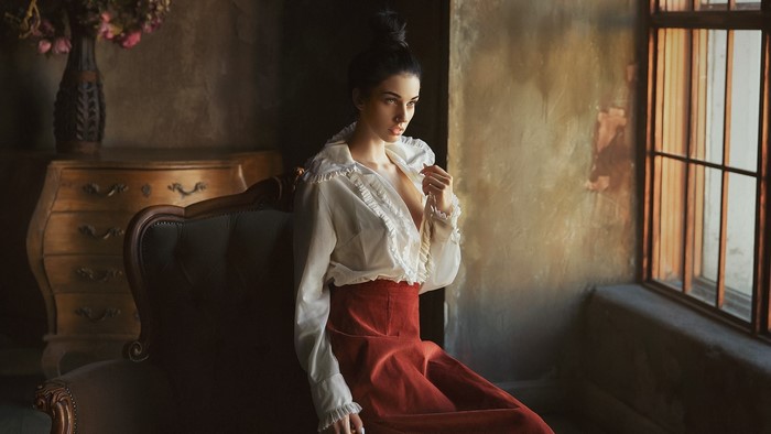 Woman in white blouse and red skirt sitting by window