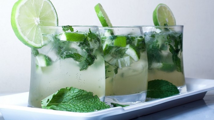 Three mojitos with lime and mint on a tray