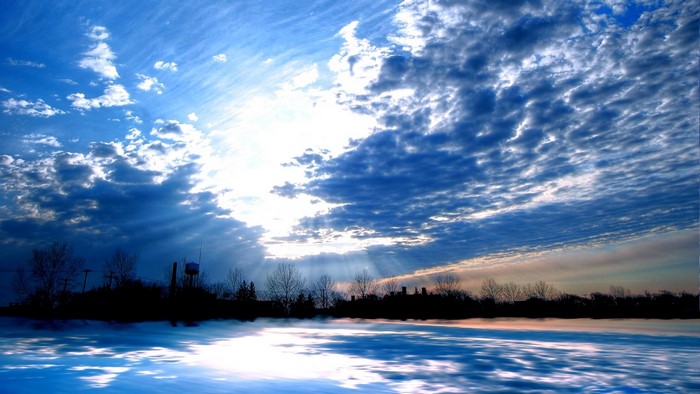 Blue Sky with Sun Rays Over Water and Silhouetted Trees