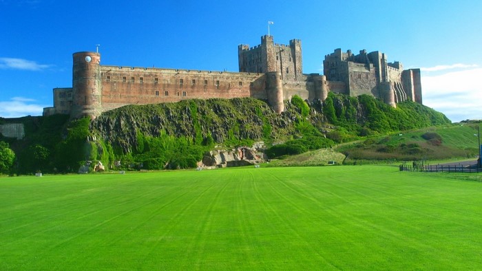 Bamburgh Castle on a grassy hill under a blue sky