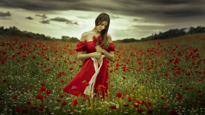 Woman in red dress holding poppies in a field