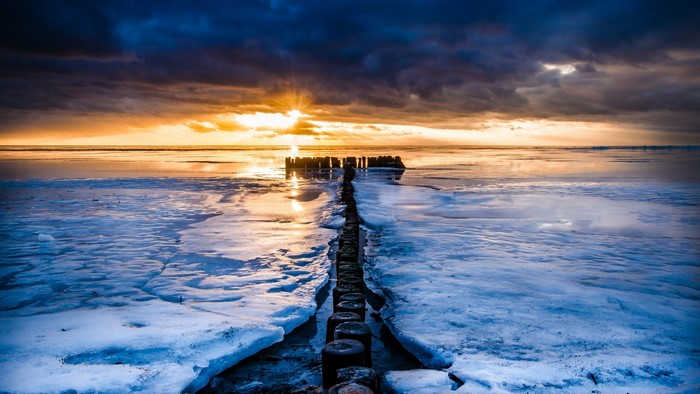 Wooden piles in icy sea at sunset