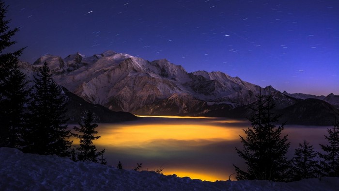 Starry night over snow-capped mountains and glowing fog