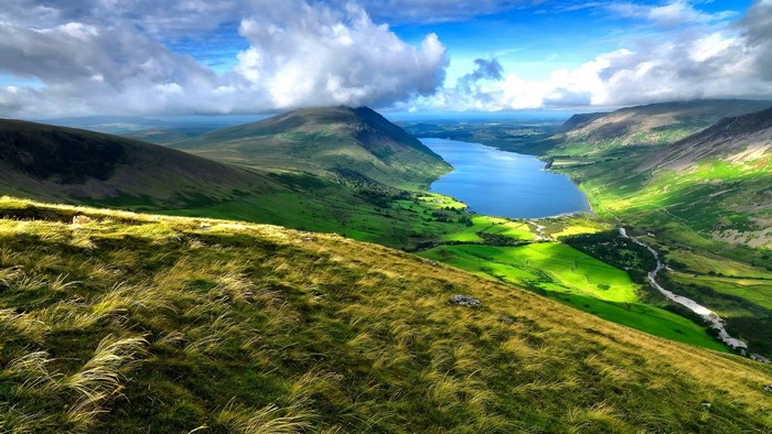 View from a grassy slope overlooking a lake and mountains