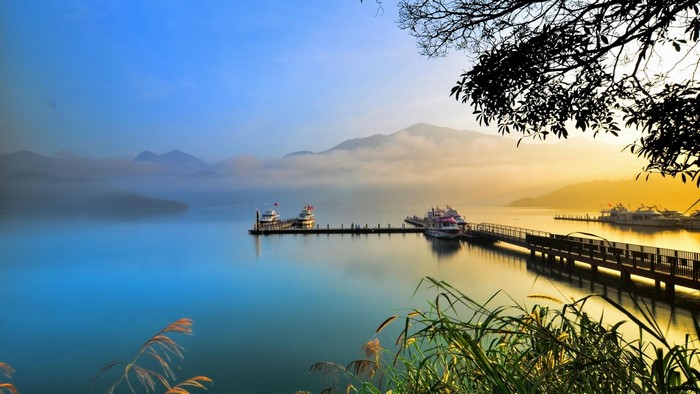 Boats docked at a pier on a misty lake at sunrise