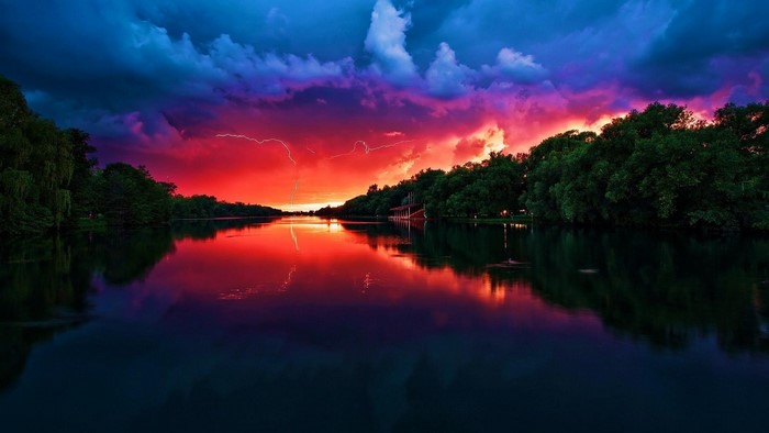 Lightning strikes over a river during a red sunset