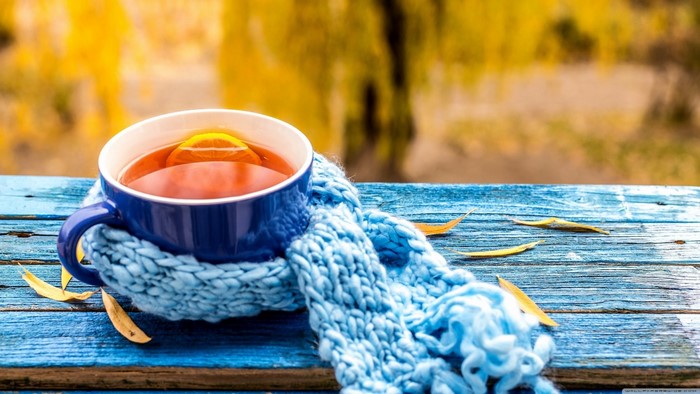 Blue mug of tea with lemon and scarf on wooden table