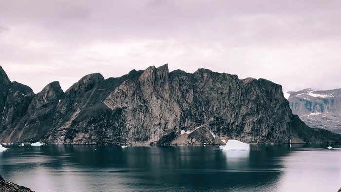 Jagged mountains rise from a dark, reflective body of water with icebergs.
