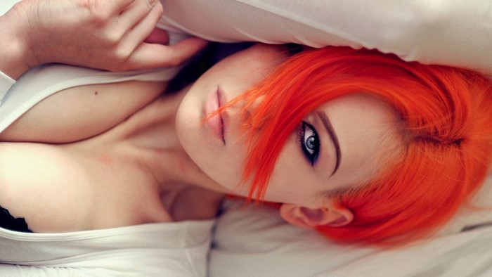 Woman with bright orange hair lying in bed