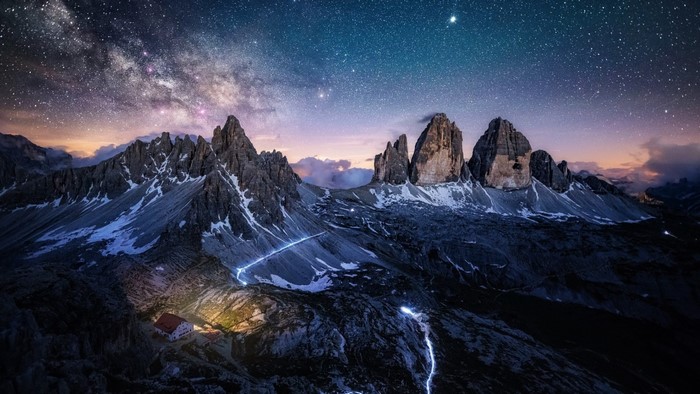 Mountain range under starry sky with a house