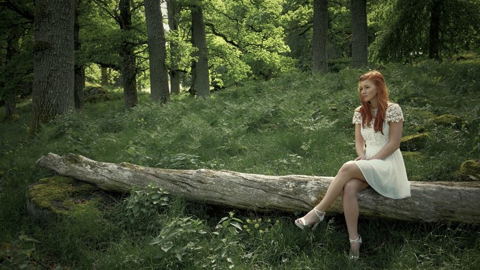 Girl in white dress sitting on a log in a forest
