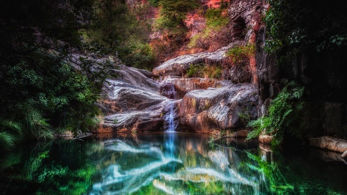 Waterfall cascading into a pool surrounded by rocks and foliage