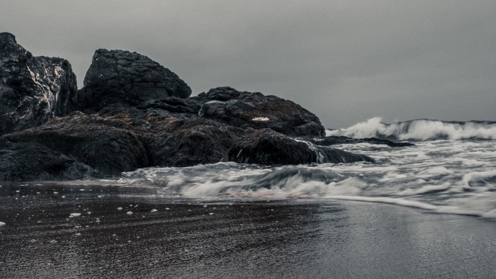 Waves crashing on rocky shore with dark sand