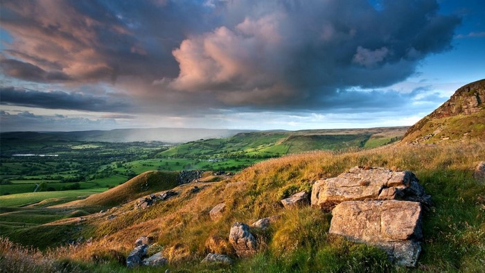 Rolling green hills and rocky outcrops under a dramatic sky