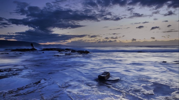 Man standing on rocks at coast during sunset