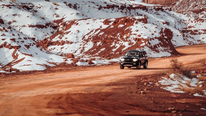 Black SUV driving on a dirt road with snow-covered red hills