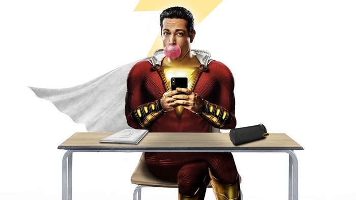 Shazam sitting at a desk blowing bubblegum