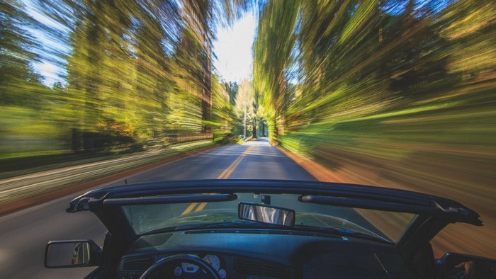 Convertible car driving on a tree-lined road