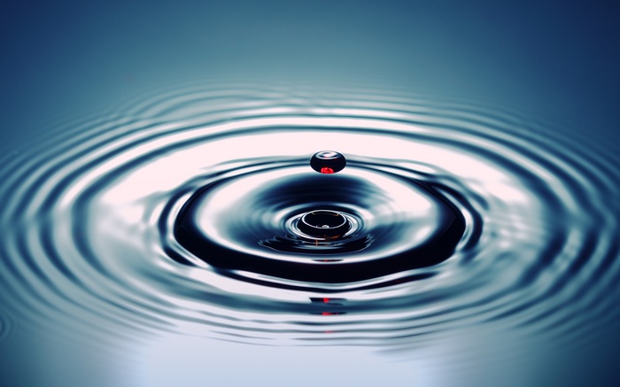 Water droplet creating ripples on a blue surface