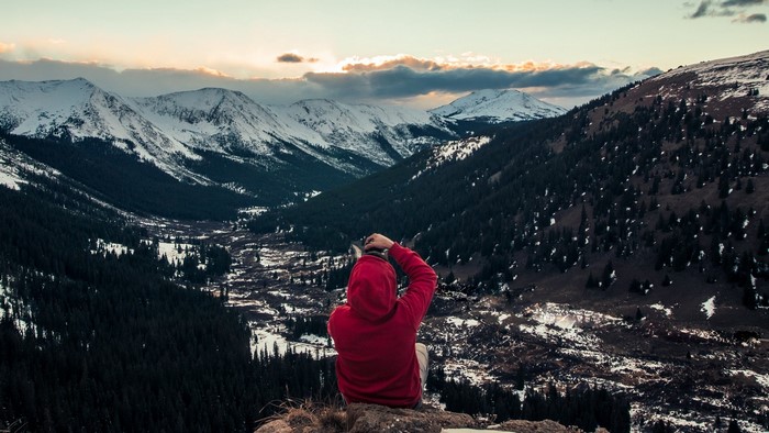 Person in red hoodie photographing snowy mountains