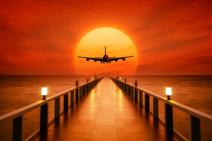 Airplane flying over pier at sunset