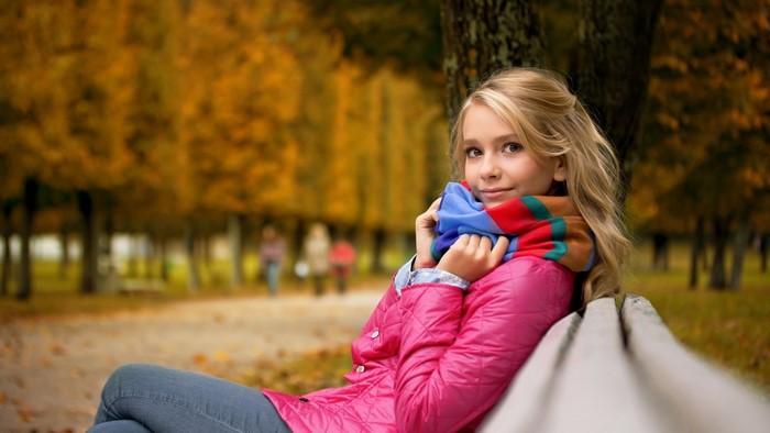 Blonde girl in pink jacket and scarf sitting on bench
