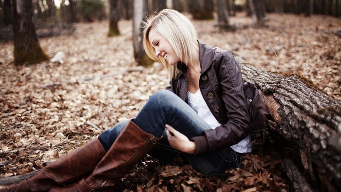 Blonde woman sitting in a forest with fallen leaves
