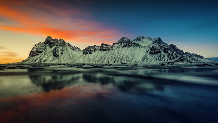 Snow-capped mountains reflected in water at sunset