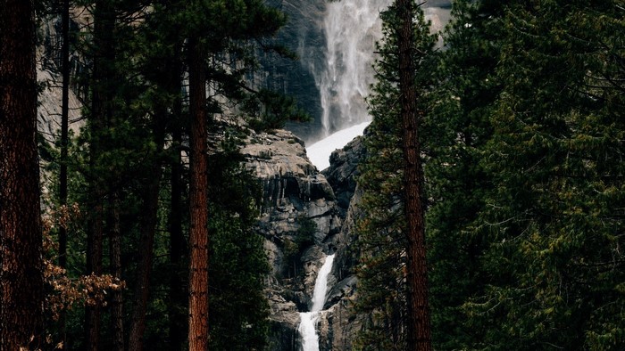 Waterfall cascading down rocky cliffs surrounded by pine trees