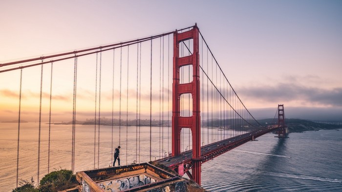 Golden Gate Bridge at sunrise with a person on the edge