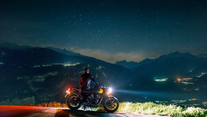 Man on motorcycle under starry sky overlooking mountains