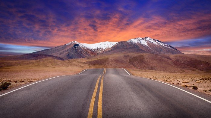 Asphalt road leading to snow-capped mountains at sunset