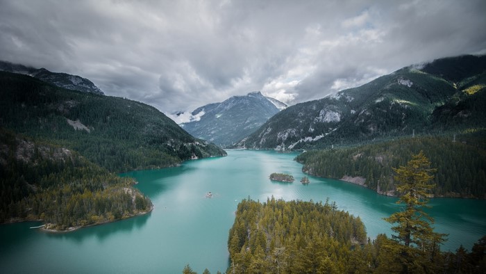 Turquoise lake surrounded by pine-covered mountains under cloudy sky
