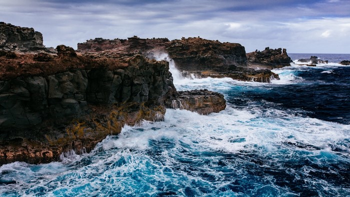 Waves crashing on rocky shore under cloudy sky