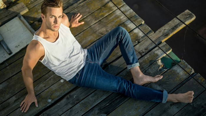 Man in white tank top and jeans on wooden dock