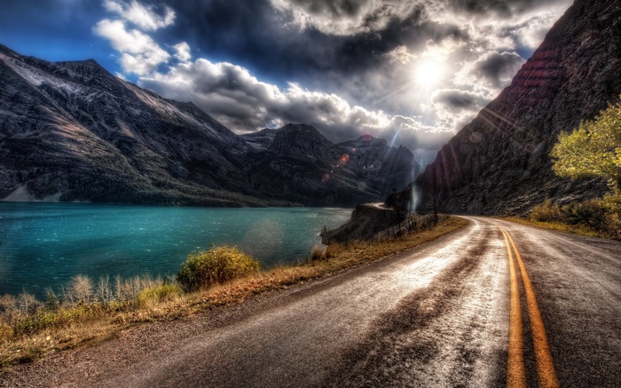 Mountain road beside a turquoise lake under dramatic clouds