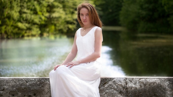 Girl in white dress sitting by water