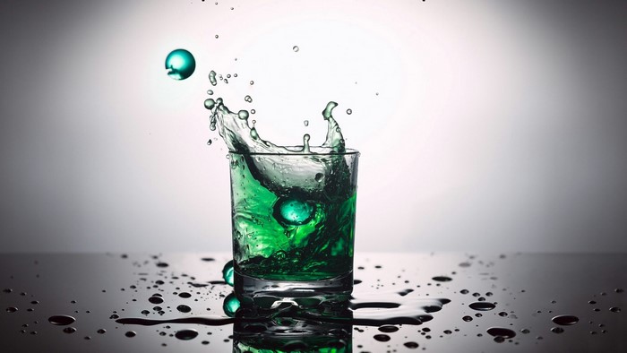 Green liquid splashing in a glass with marbles