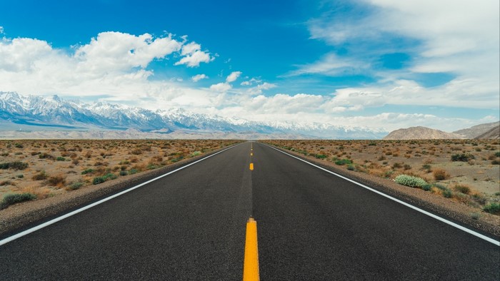 Desert road with snow-capped mountains under a blue sky